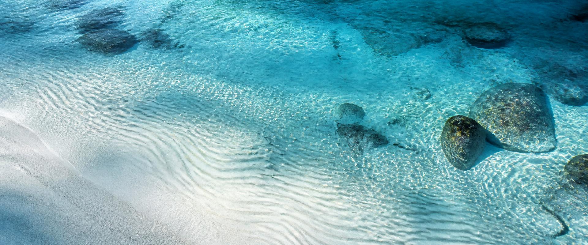 Aerial view of clear glacial water rippling over white sand
